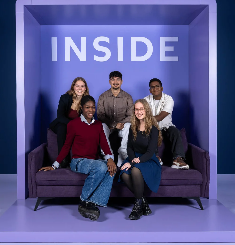 Fünf Personen sitzen und stehen in einem lila Rahmen mit dem Wort „INSIDE“ oben. Sie sind lächelnd und entspannt auf einem Sofa positioniert.