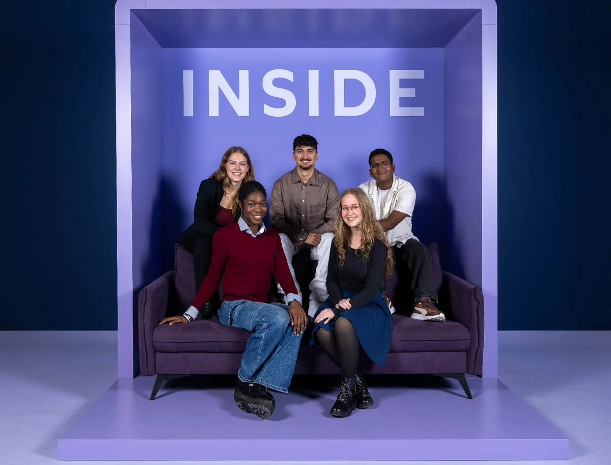 Fünf Personen sitzen und stehen in einem lila Rahmen mit dem Wort „INSIDE“ oben. Sie sind lächelnd und entspannt auf einem Sofa positioniert.