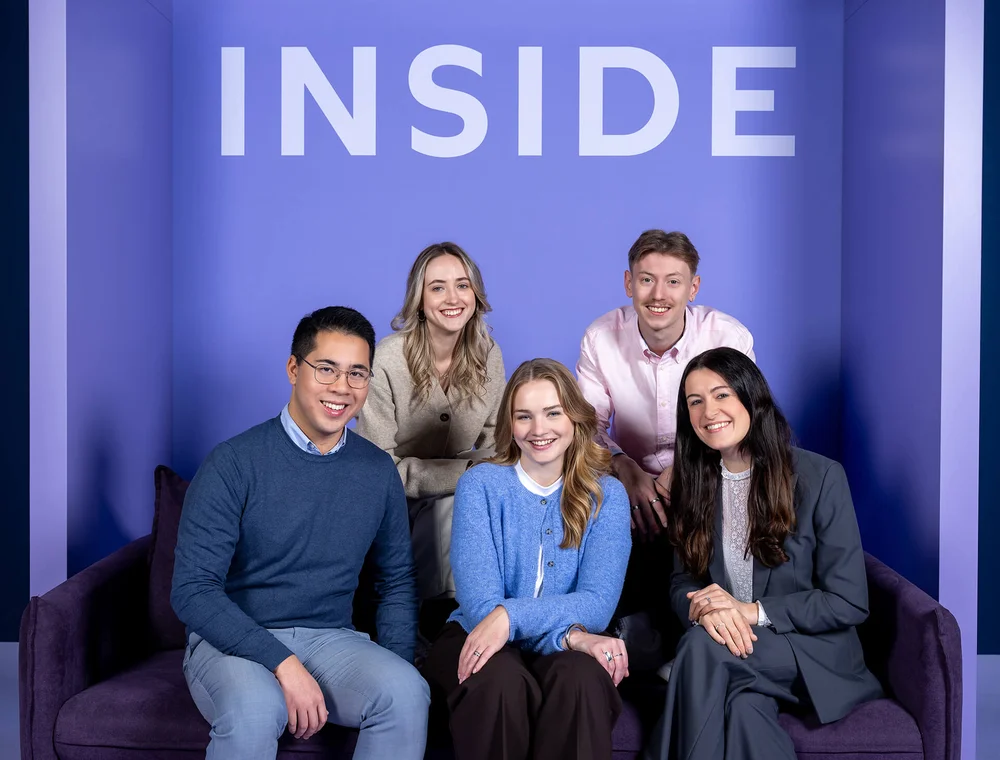 Fünf Personen sitzen und stehen vor einem lila Hintergrund mit dem Wort "INSIDE". Sie lächeln in die Kamera und wirken freundlich und professionell.