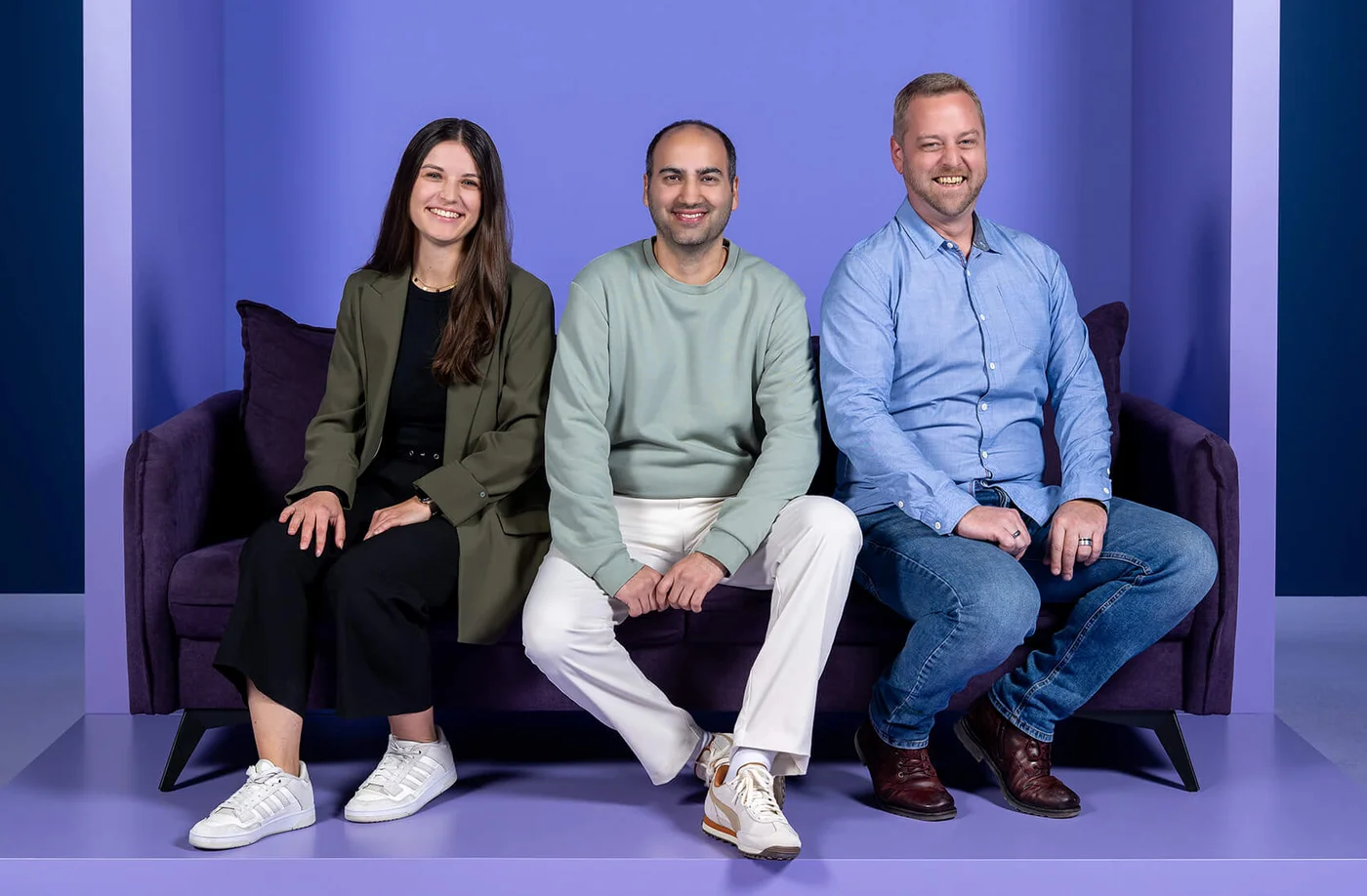 Drei Personen sitzen auf einem Sofa vor einem lila Hintergrund. Hinter ihnen steht in großen Buchstaben der Schriftzug "INSIDE". Alle drei lächeln und schauen in die Kamera.