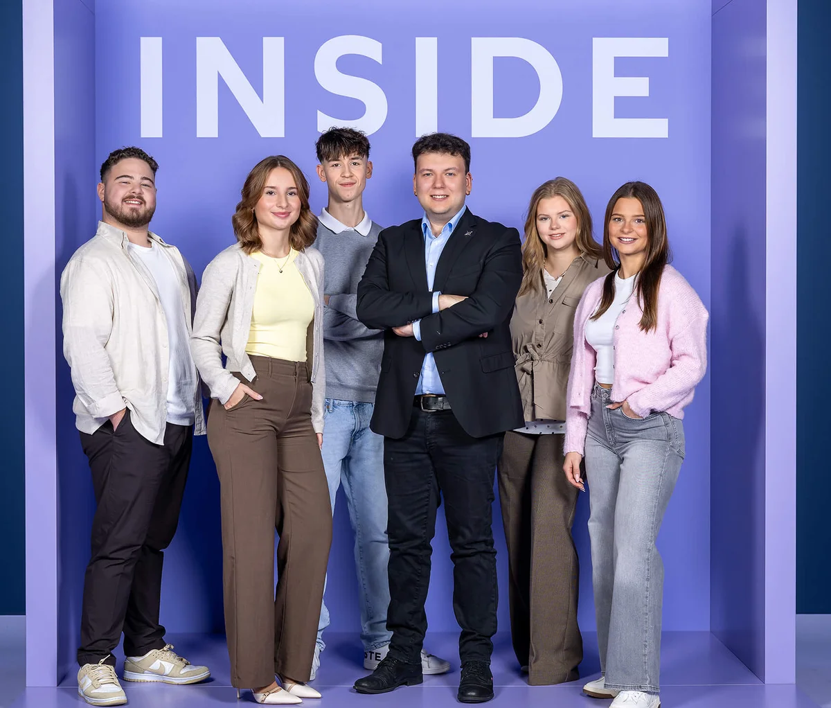 Sechs Personen stehen nebeneinander vor einem lila Hintergrund mit dem Wort "INSIDE" darüber. Die Gruppe wirkt freundlich und professionell.