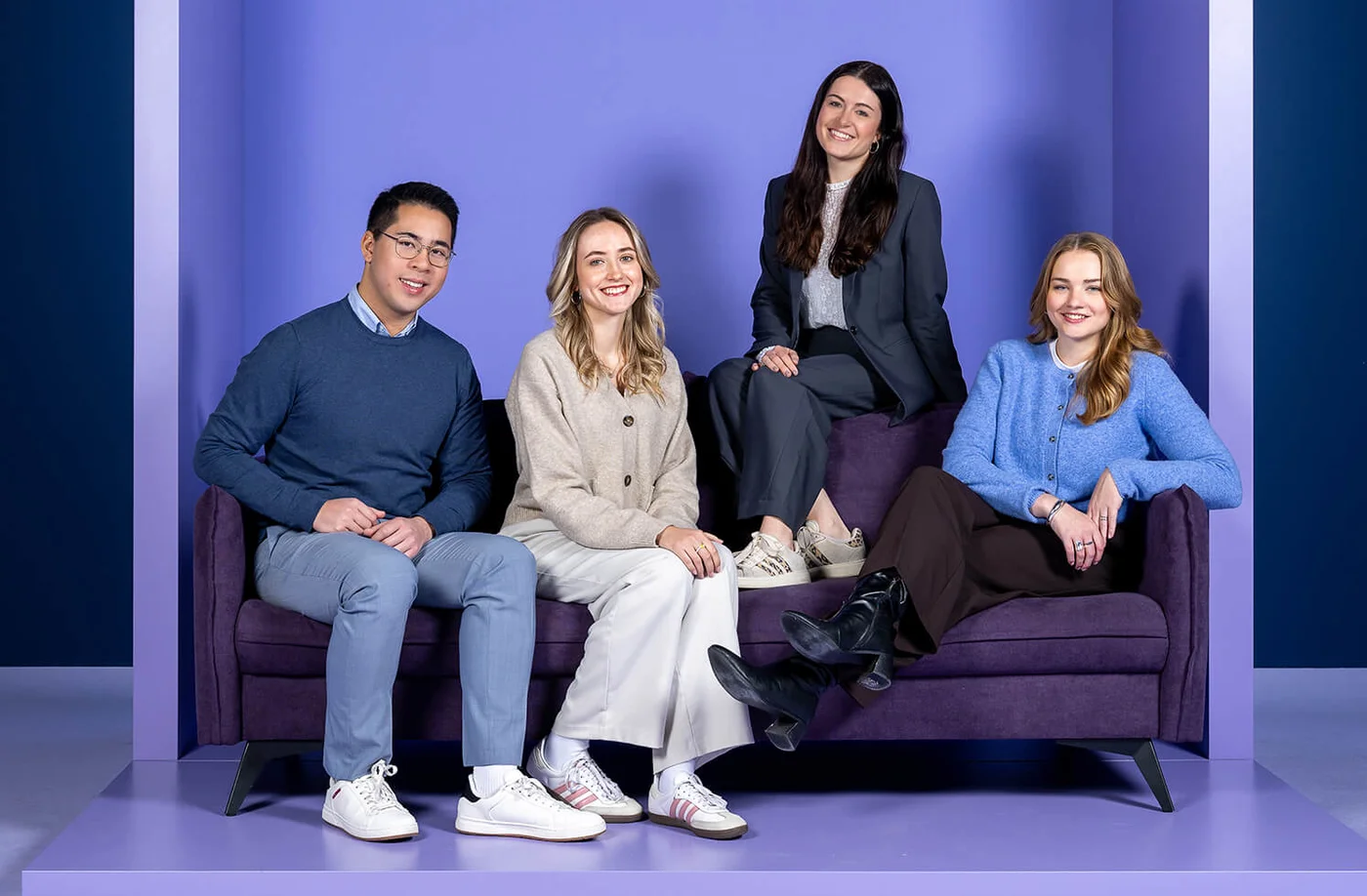 Es tut mir leid, ich weiß nicht, wer auf dem Bild ist. Ein Mann und drei Frauen sitzen auf einem Sofa in einer lila Box. Oben steht das Wort „INSIDE“. Alle lächeln in die Kamera.